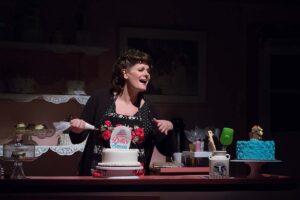 woman singing, while decorating cake, during a play