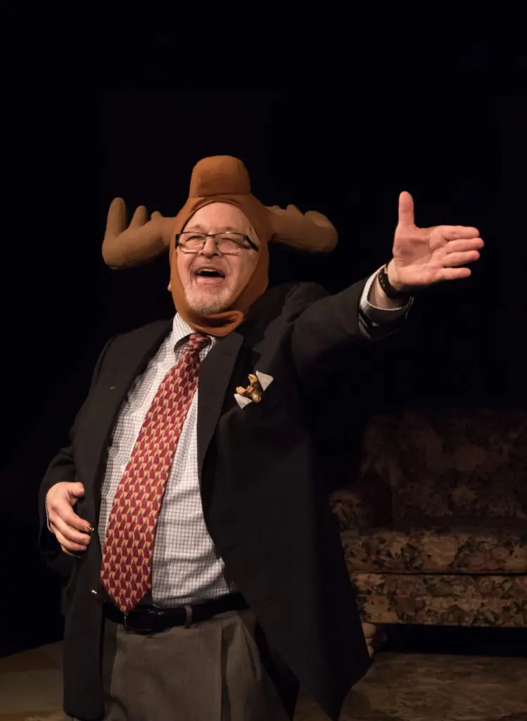 A person wearing a moose hat, and a suit, smiling and gesturing to the crowd